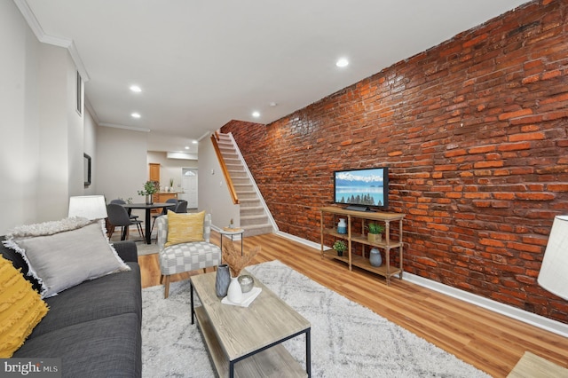 living room featuring brick wall, crown molding, and light hardwood / wood-style flooring