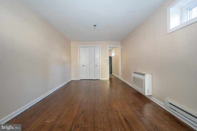 empty room with dark hardwood / wood-style flooring, a wall mounted AC, and a baseboard heating unit