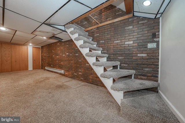 basement with baseboard heating, a paneled ceiling, brick wall, wooden walls, and carpet flooring