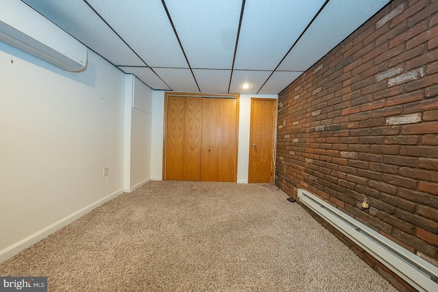 basement featuring baseboard heating, brick wall, a paneled ceiling, and carpet