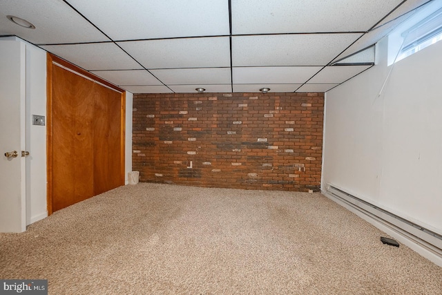 basement featuring brick wall, a baseboard heating unit, a drop ceiling, and carpet