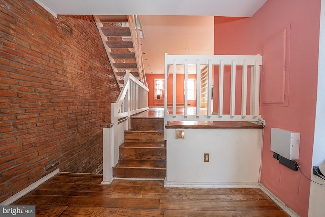 staircase with brick wall and wood-type flooring