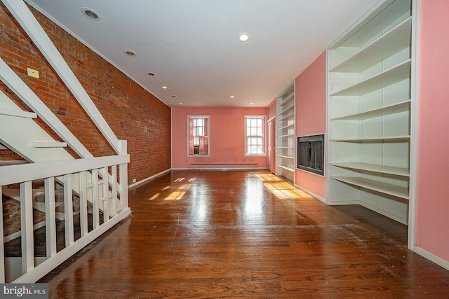 unfurnished living room featuring brick wall, dark hardwood / wood-style flooring, and built in shelves