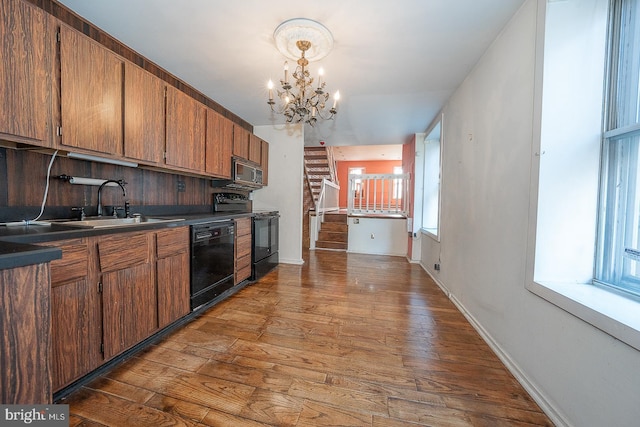 kitchen featuring hardwood / wood-style floors, black appliances, a notable chandelier, pendant lighting, and sink