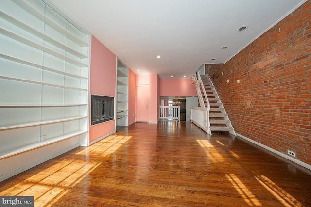 unfurnished living room with built in shelves, hardwood / wood-style floors, and brick wall