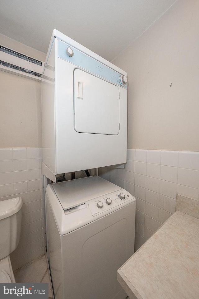 laundry room featuring tile walls, light tile patterned floors, and stacked washer / dryer