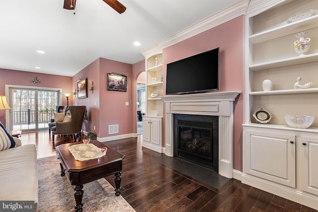 living room with built in shelves, ceiling fan, dark hardwood / wood-style flooring, and ornamental molding