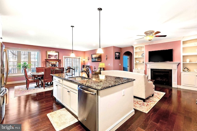 kitchen with sink, decorative light fixtures, dark stone countertops, stainless steel dishwasher, and a kitchen island with sink