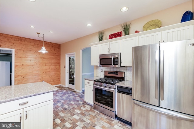 kitchen featuring light stone counters, decorative light fixtures, stainless steel appliances, wood walls, and white cabinets