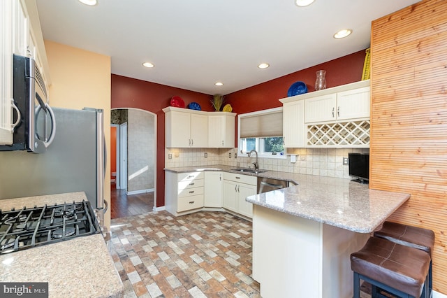 kitchen featuring sink, white cabinetry, kitchen peninsula, a breakfast bar area, and appliances with stainless steel finishes