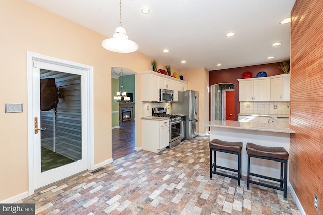 kitchen with white cabinets, tasteful backsplash, kitchen peninsula, and appliances with stainless steel finishes