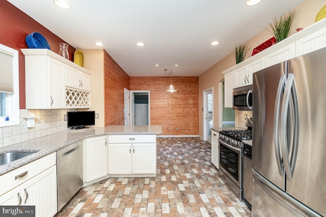 kitchen featuring stainless steel appliances, wooden walls, white cabinetry, decorative light fixtures, and kitchen peninsula