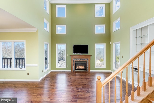 unfurnished living room featuring a high end fireplace, dark hardwood / wood-style flooring, a towering ceiling, and a healthy amount of sunlight