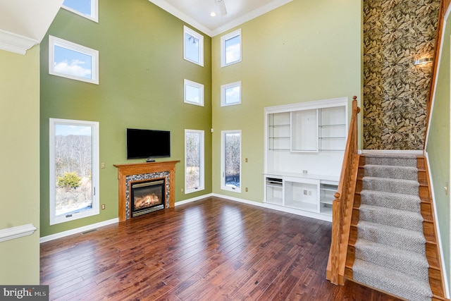 unfurnished living room featuring a towering ceiling, a high end fireplace, ornamental molding, and dark wood-type flooring