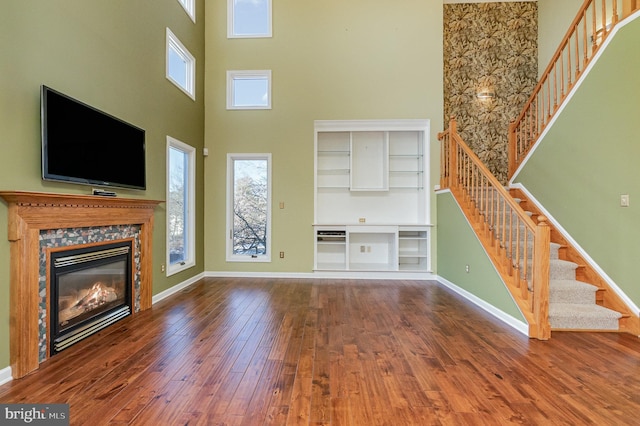 unfurnished living room with a towering ceiling, a high end fireplace, hardwood / wood-style flooring, and plenty of natural light