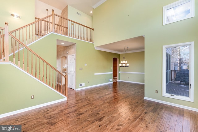 unfurnished living room with ornamental molding, a towering ceiling, and hardwood / wood-style flooring