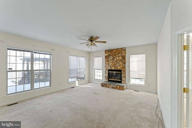 unfurnished living room with ceiling fan, a healthy amount of sunlight, light colored carpet, and a stone fireplace