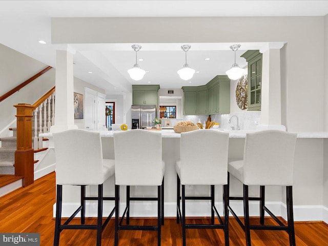 kitchen with a kitchen bar, green cabinetry, stainless steel fridge, kitchen peninsula, and hardwood / wood-style flooring