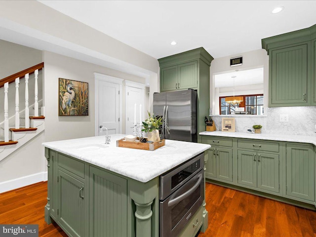 kitchen with stainless steel appliances, green cabinets, dark hardwood / wood-style flooring, sink, and a kitchen island with sink