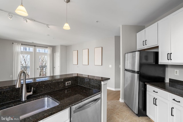 kitchen with sink, appliances with stainless steel finishes, dark stone countertops, white cabinetry, and decorative light fixtures