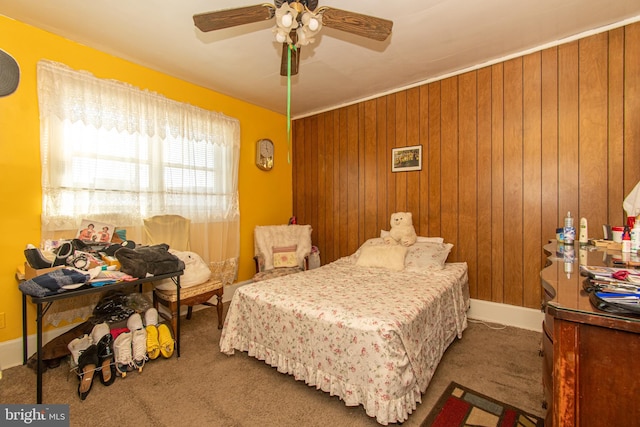 bedroom featuring ceiling fan, wood walls, and carpet