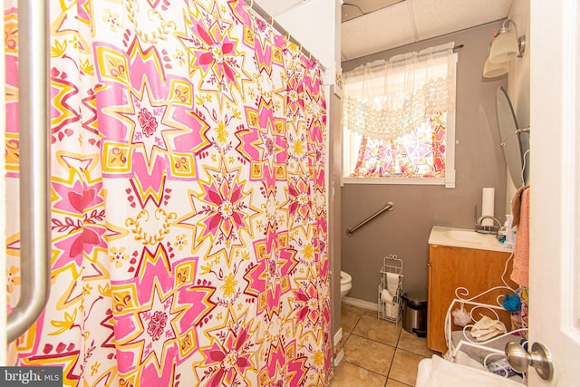 bathroom with tile patterned flooring, toilet, walk in shower, a paneled ceiling, and vanity