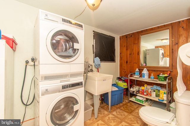 laundry room featuring stacked washing maching and dryer and wood walls