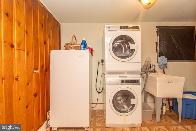 laundry area with light parquet flooring and stacked washing maching and dryer