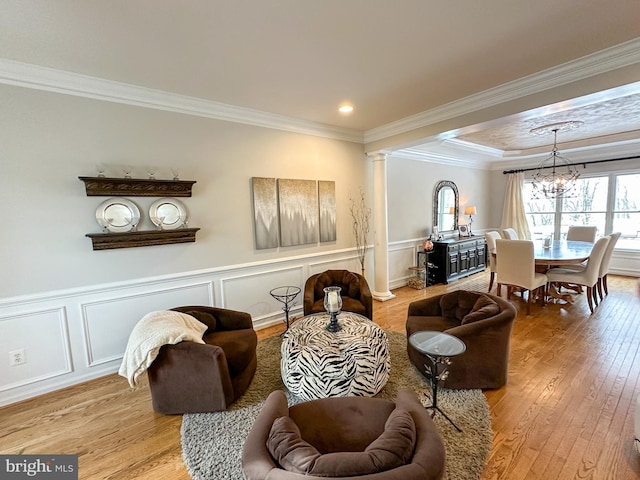 living room featuring an inviting chandelier, crown molding, light wood-type flooring, and ornate columns