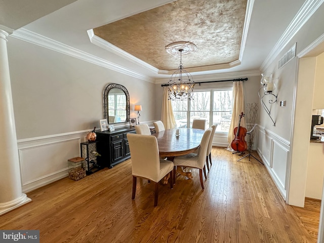 dining room with a chandelier, ornamental molding, a tray ceiling, hardwood / wood-style flooring, and decorative columns