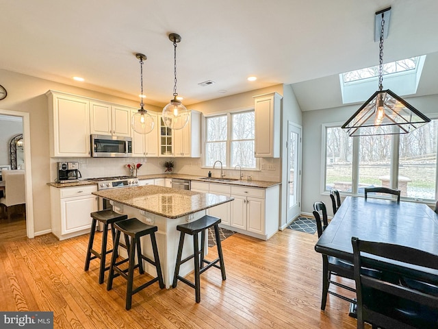 kitchen featuring sink, appliances with stainless steel finishes, hanging light fixtures, a center island, and light stone countertops