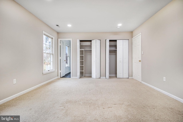 unfurnished bedroom featuring two closets and light carpet