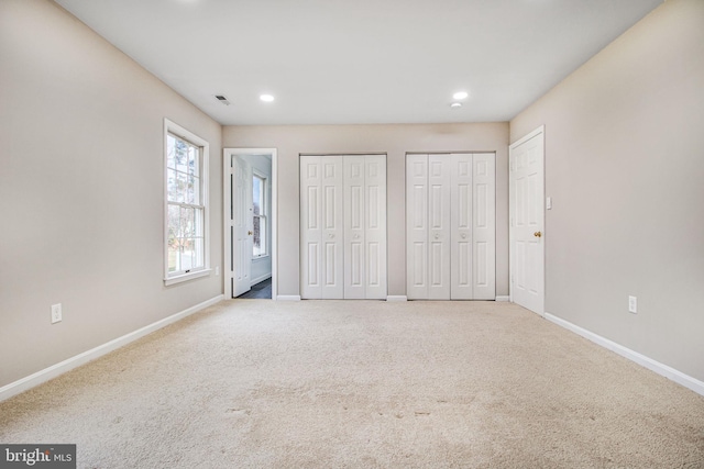 unfurnished bedroom with two closets and light colored carpet