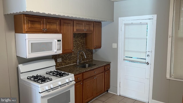 kitchen featuring white appliances, dark stone countertops, sink, and light tile patterned floors