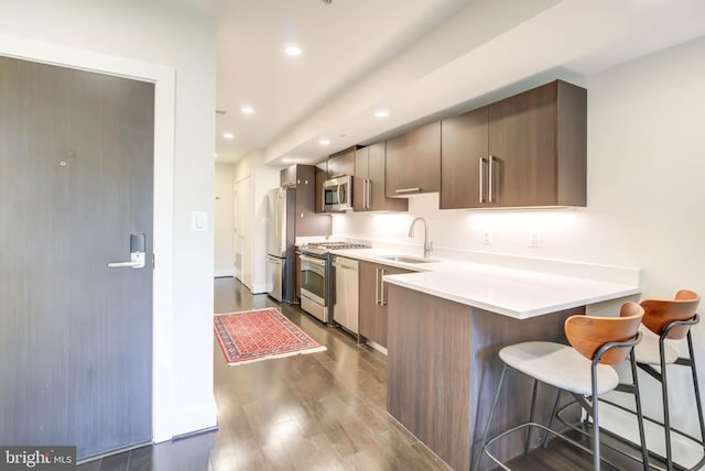 kitchen featuring dark hardwood / wood-style floors, sink, a breakfast bar area, kitchen peninsula, and stainless steel appliances