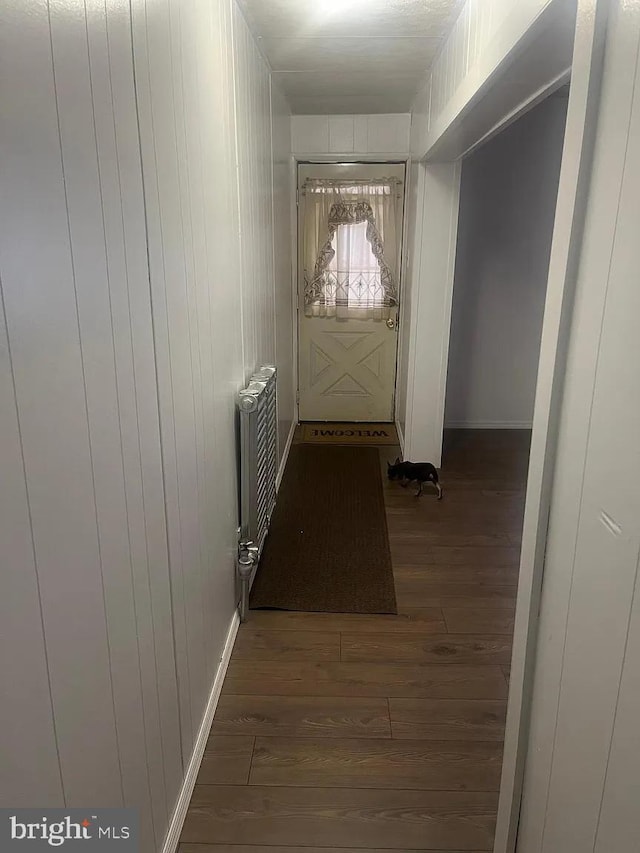 corridor featuring radiator heating unit, dark hardwood / wood-style flooring, and wood walls