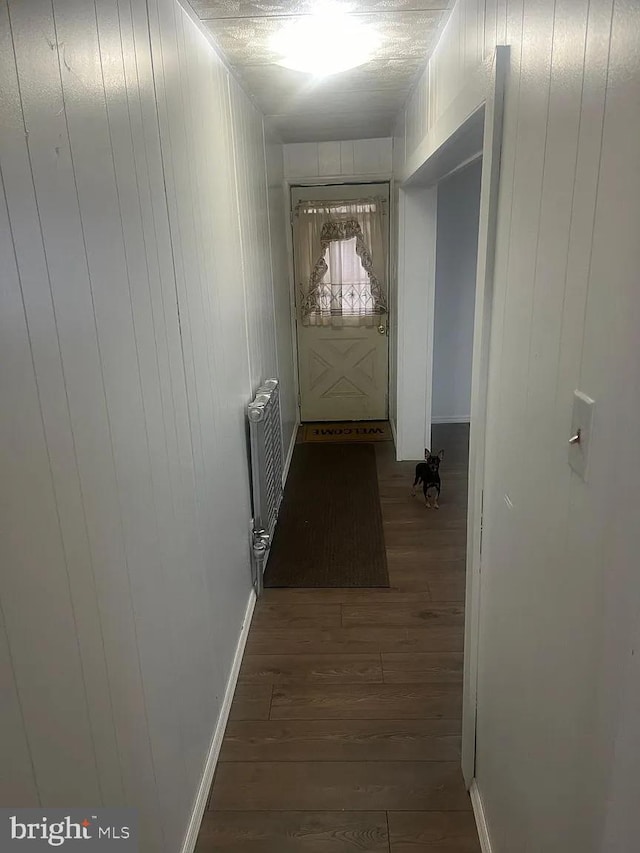 hallway with dark wood-type flooring, radiator heating unit, and wood walls