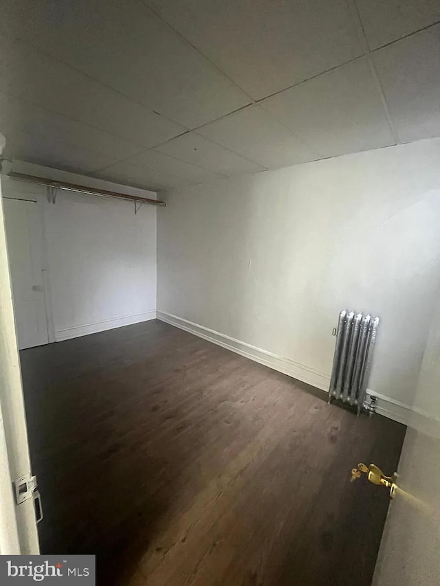 empty room with radiator, a paneled ceiling, and dark hardwood / wood-style flooring