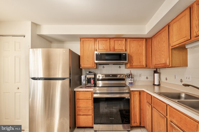 kitchen featuring a sink, light countertops, appliances with stainless steel finishes, backsplash, and brown cabinets