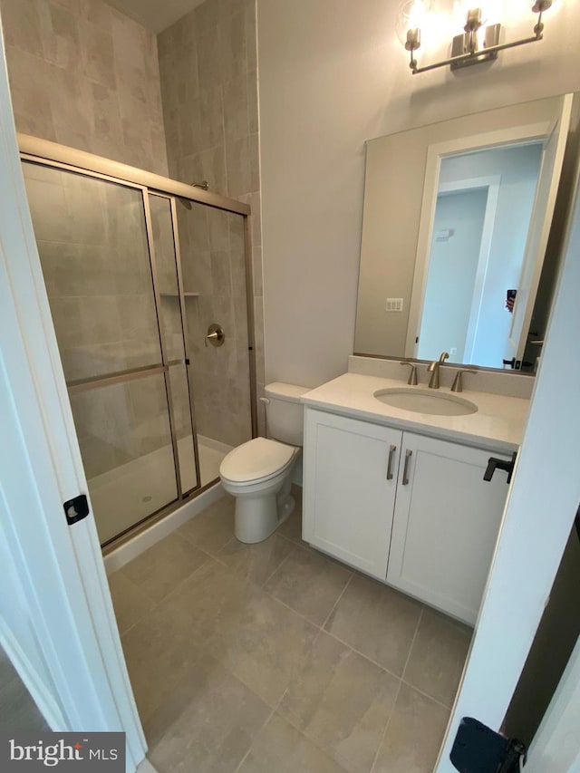 bathroom featuring toilet, vanity, tile patterned flooring, and a shower with shower door