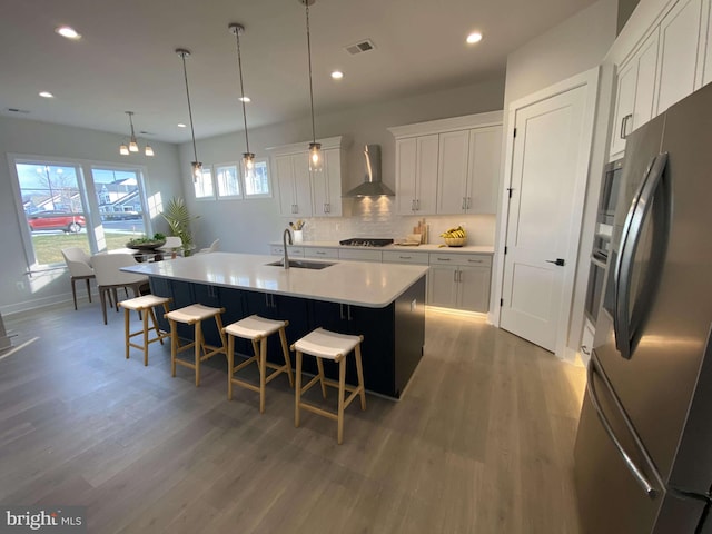 kitchen featuring appliances with stainless steel finishes, white cabinetry, an island with sink, and wall chimney exhaust hood