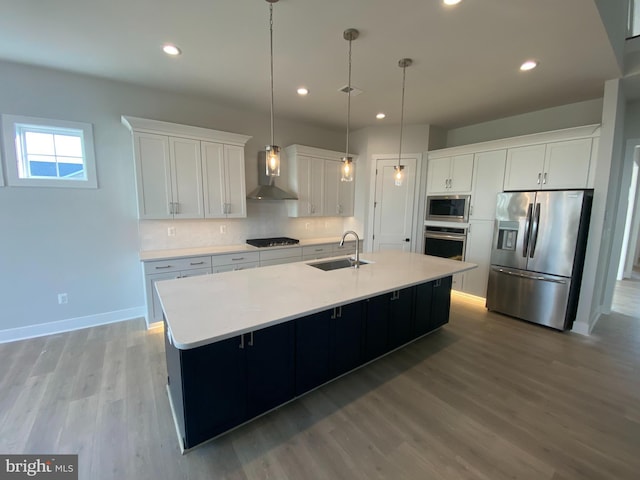 kitchen featuring appliances with stainless steel finishes, white cabinetry, a center island with sink, and wall chimney exhaust hood