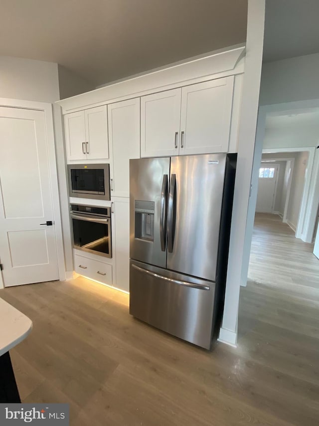 kitchen with white cabinets, appliances with stainless steel finishes, and hardwood / wood-style flooring