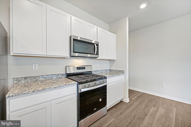 kitchen with white cabinetry, light wood-type flooring, light stone counters, and appliances with stainless steel finishes