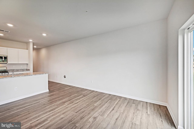 kitchen with light stone countertops, light hardwood / wood-style flooring, white cabinets, appliances with stainless steel finishes, and sink