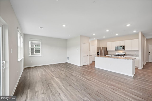 kitchen featuring white cabinetry, a kitchen island with sink, stainless steel appliances, light stone counters, and light hardwood / wood-style flooring