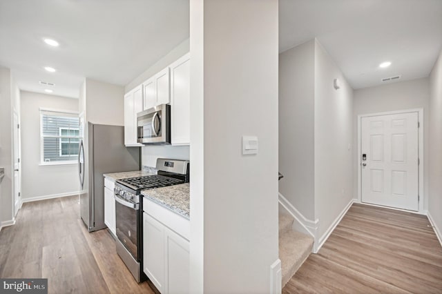 kitchen with light stone counters, white cabinets, light wood-type flooring, and appliances with stainless steel finishes