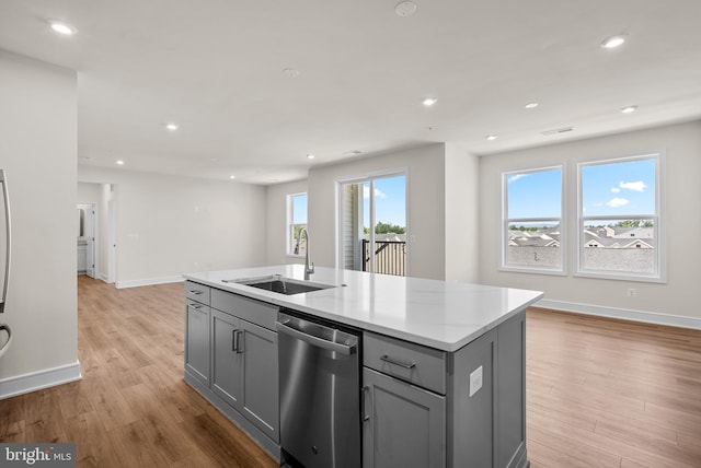 kitchen with an island with sink, stainless steel dishwasher, gray cabinetry, and sink