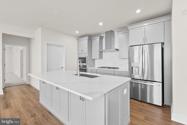 kitchen with light stone countertops, wall chimney exhaust hood, a large island, appliances with stainless steel finishes, and sink