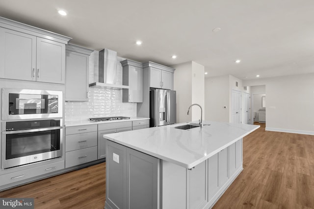 kitchen with stainless steel appliances, sink, a center island with sink, wall chimney range hood, and gray cabinetry